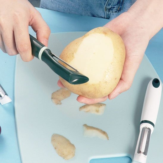 Couteau économe vert pelant une pomme de terre